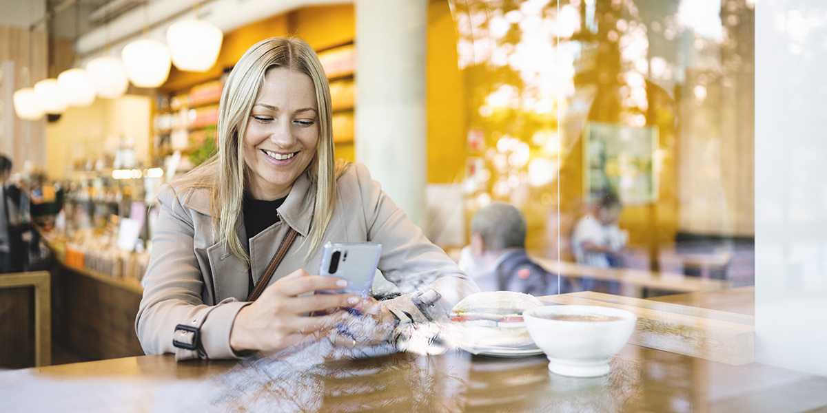 Bilde av kvinne som surfer trygt på mobilen, mens hun sitter på kafé