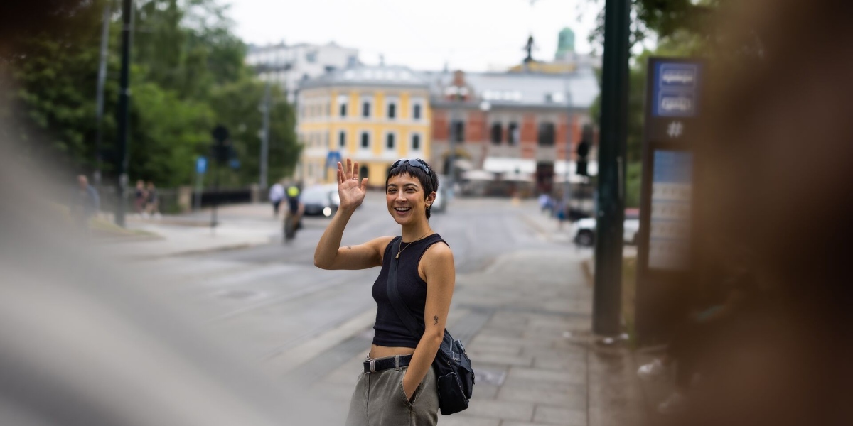 Ung kvinne som står på et busstopp og vinker til fotografen